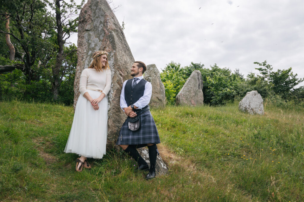 Newlyweds are posing by the rock on Bornholm island during their elopement abroad to Scandinavia.